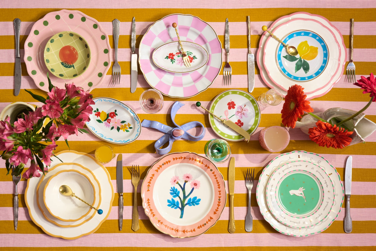 Mesa posta super colorida com os pratos da marca Bitossi, talheres e copos, com flores coloridas compondo a decoração.