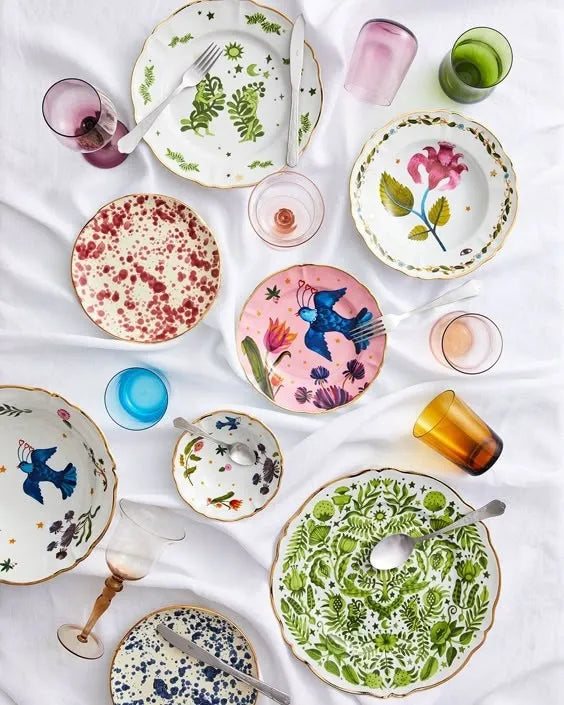 Exposição de pratos de diversas coleções da marca Bitossi, com copos coloridos ao redor e talheres.