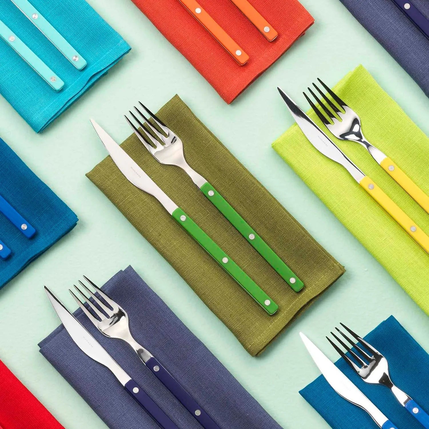 Composição colorida de talheres da marca Bugatti italy sobre guardanapos da mesma cor.