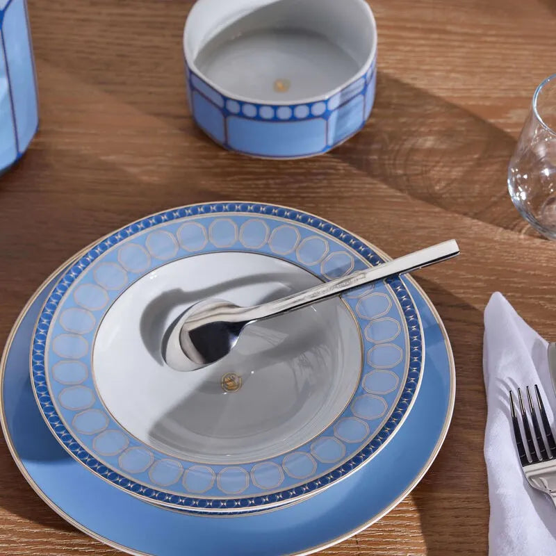 Mesa de madeira com itens e pratos da marca Rosenthal, talheres e copos de vidro.