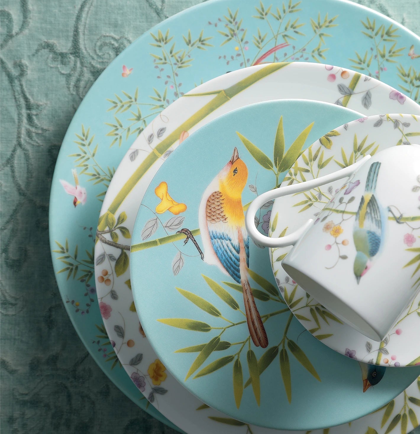 Coleção de pratos e xícara Paradis da marca Raynaud Limoges, sobre toalha azul bordada.