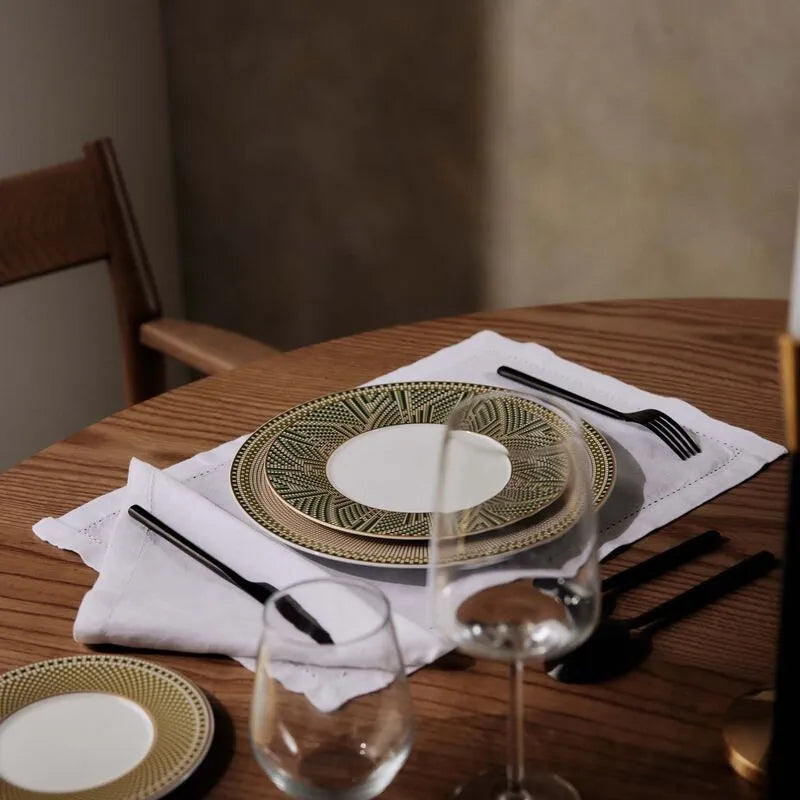 Mesa posta com prato, talheres, taças e guardanapos, sobre uma mesa de madeira.