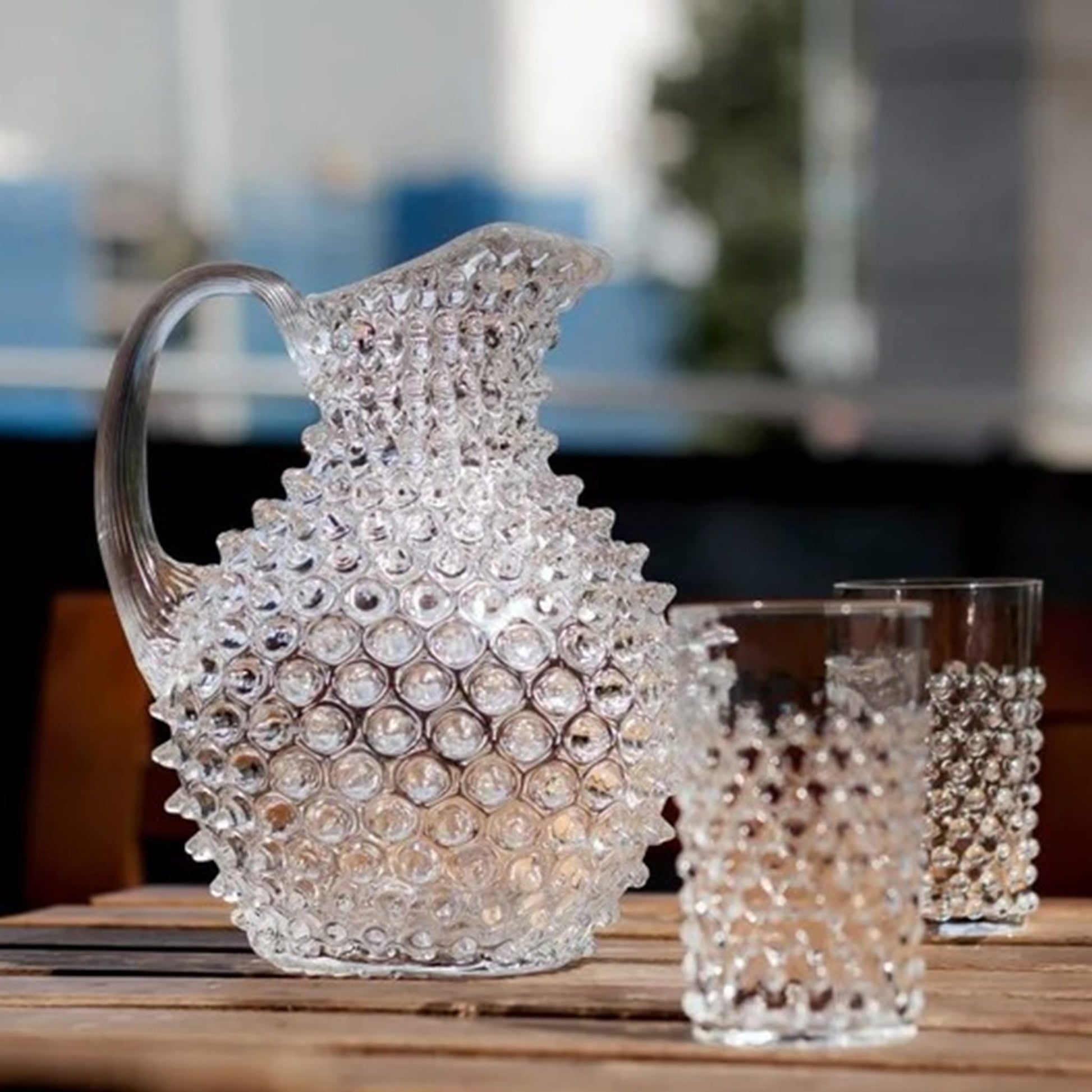 Copo Curto Hobnail Cristal com uma jarra da mesma coleção, em cima de uma mesa.