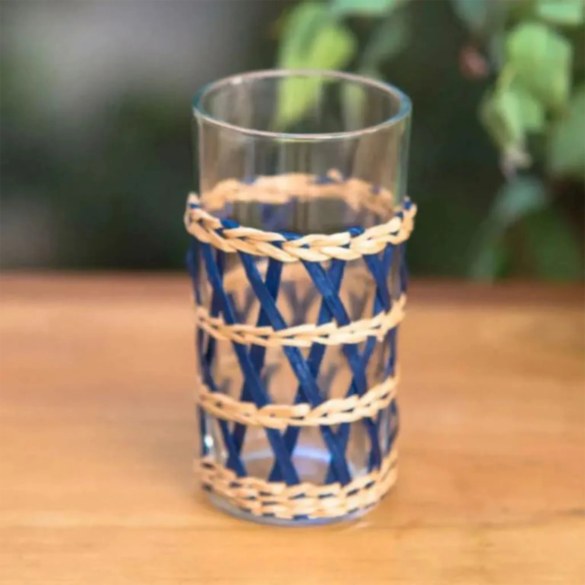 Copo Long Drink Rattan Azul em cima de uma mesa de madeira com plantas ao fundo.