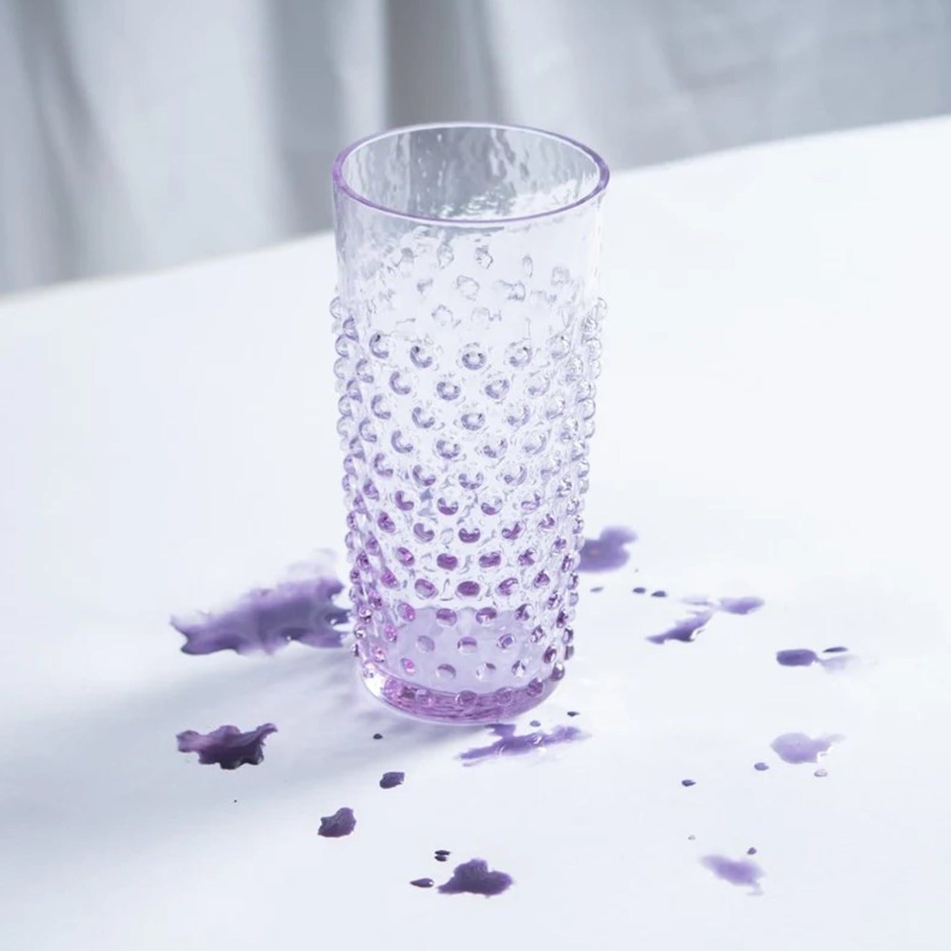 Copo Longo Hobnail Lilás em cima de uma mesa branca com tinta lilás ao redor.