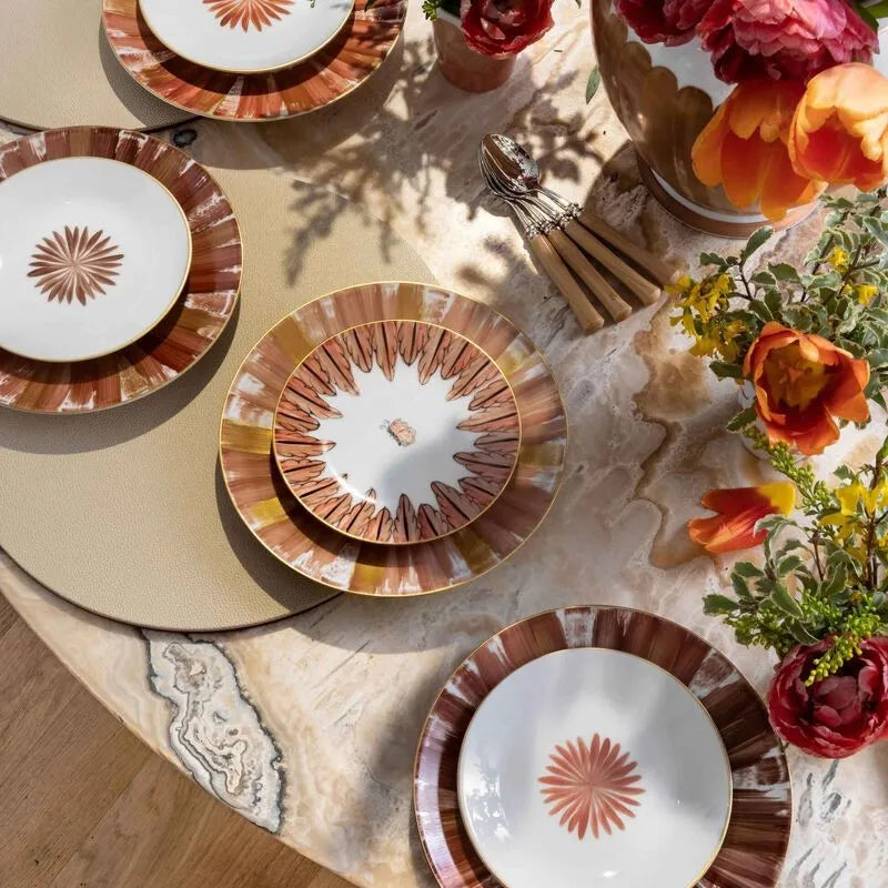 Mesa de pedra com pratos da marca Marie Dâage Paris e flores laranjas com vermelha.