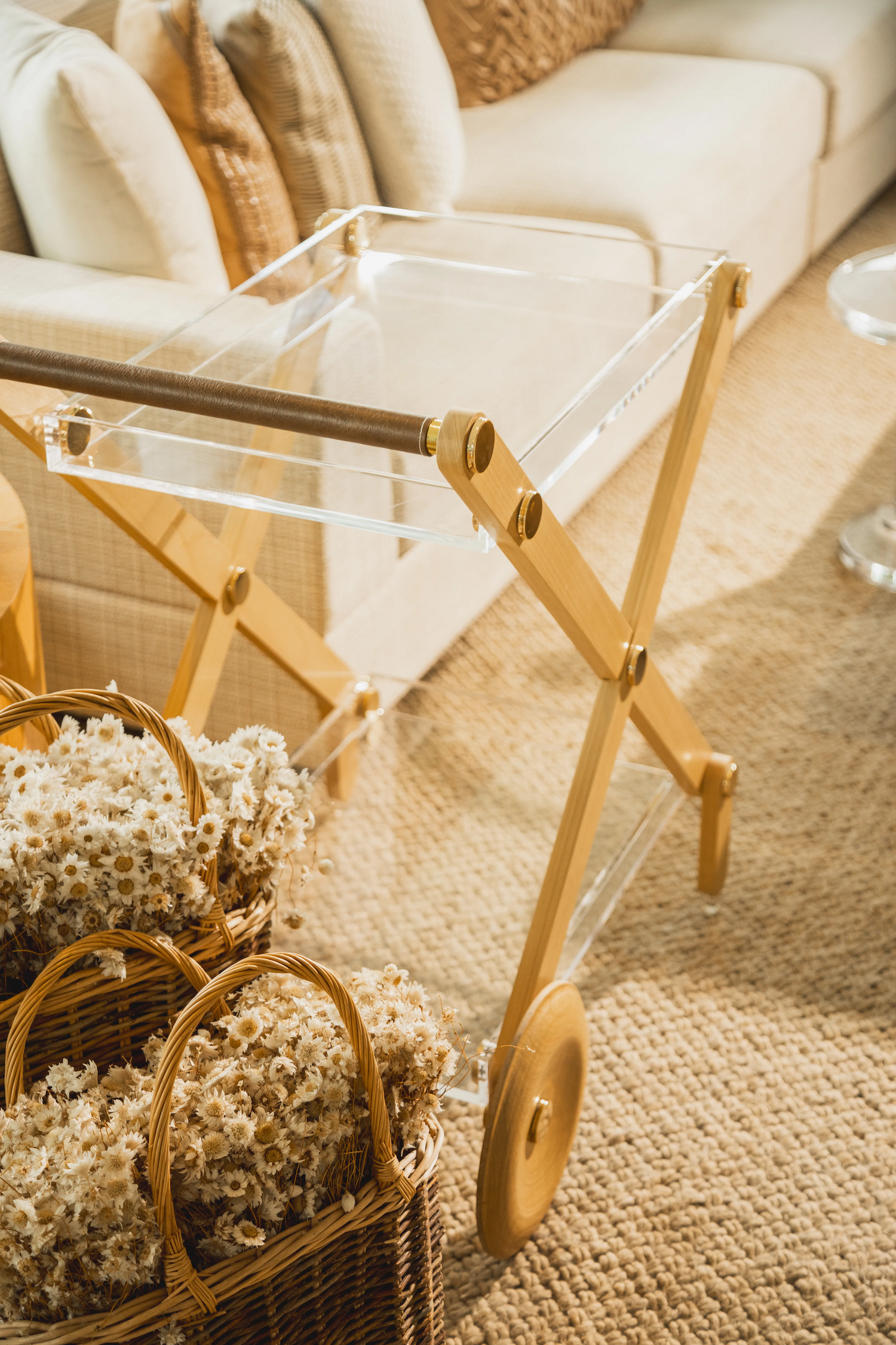 Carrinho de bar da marca Onom Design ambientado numa sala com tapete, sofá claro, almofadas claras e flores.