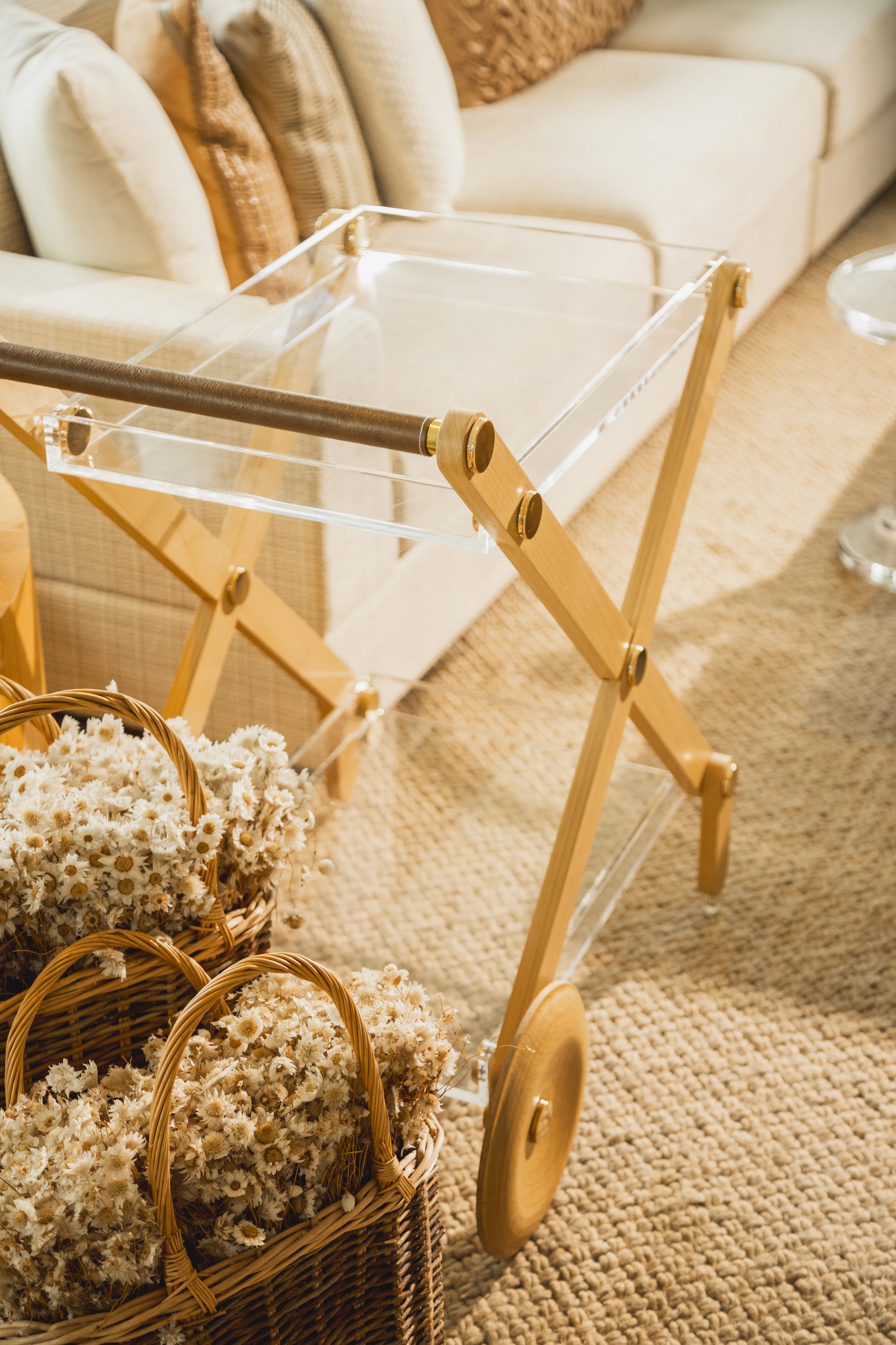 Carrinho de bar da marca Onom Design ambientado numa sala com tapete, sofá claro, almofadas claras e flores.