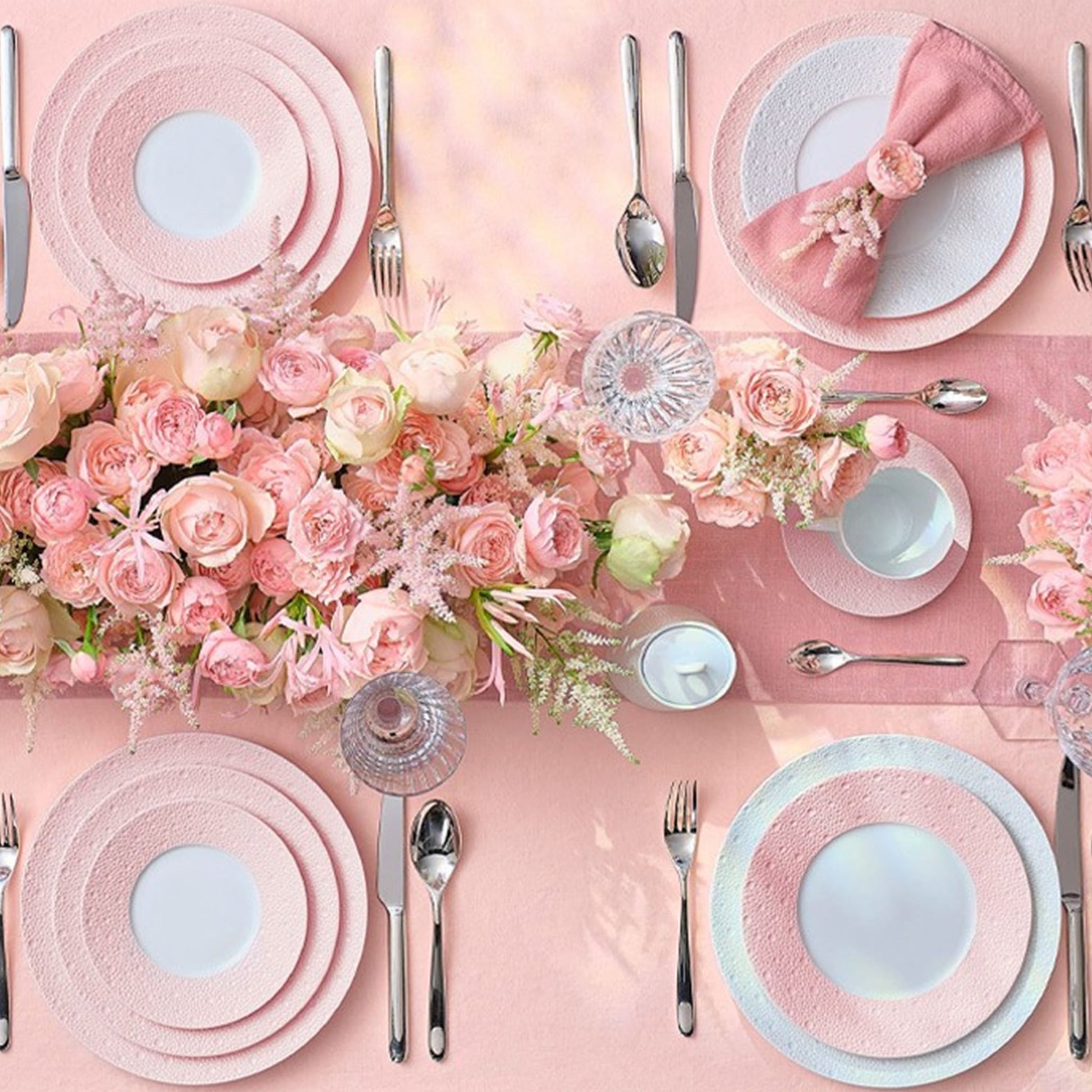 Cena ambientada em mesa cheia de flores rosas e adornos no mesmo tom, com os pratos da coleção Ecume Rosa.