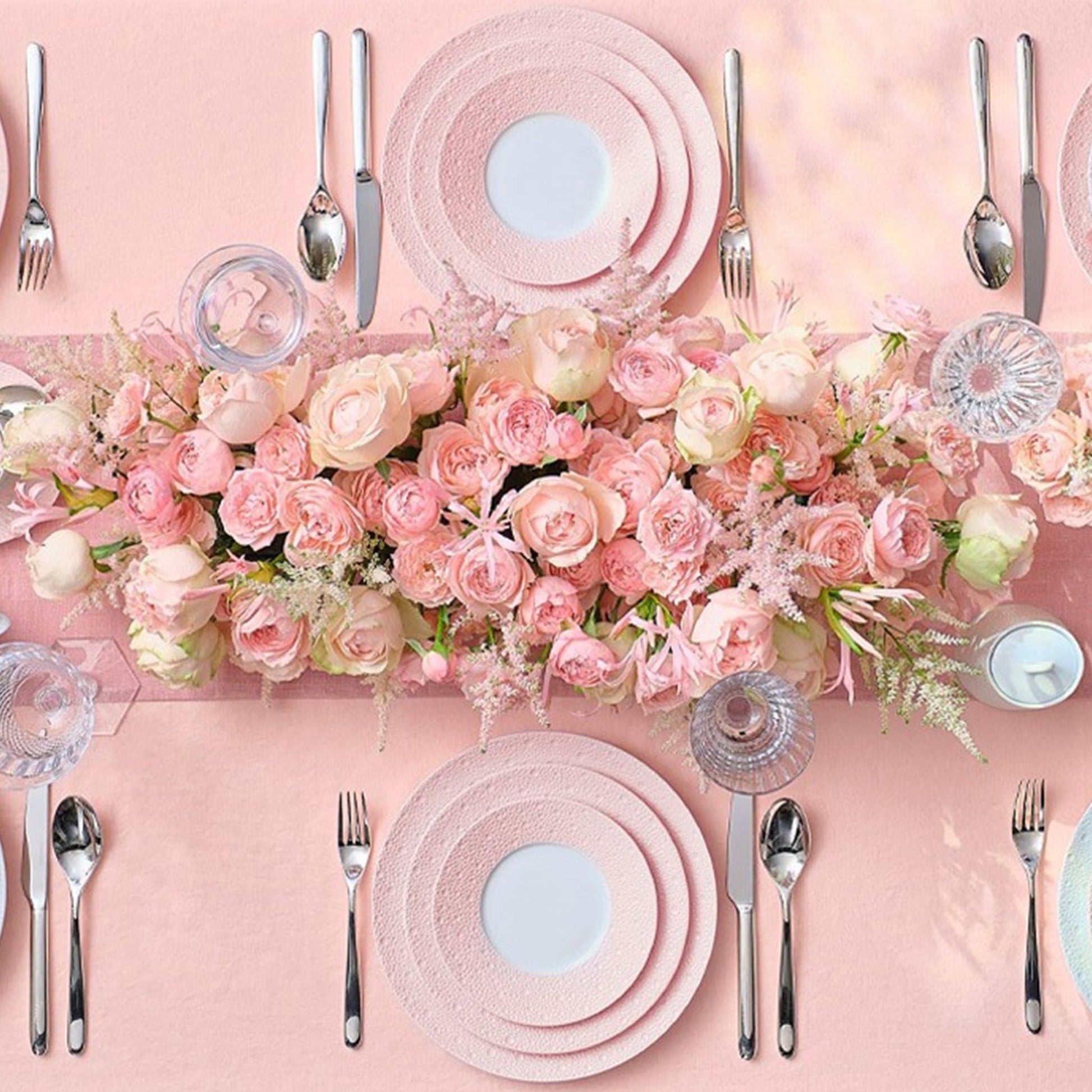 Cena ambientada em mesa, com flores rosas e com pratos da coleção Ecume Rosa.