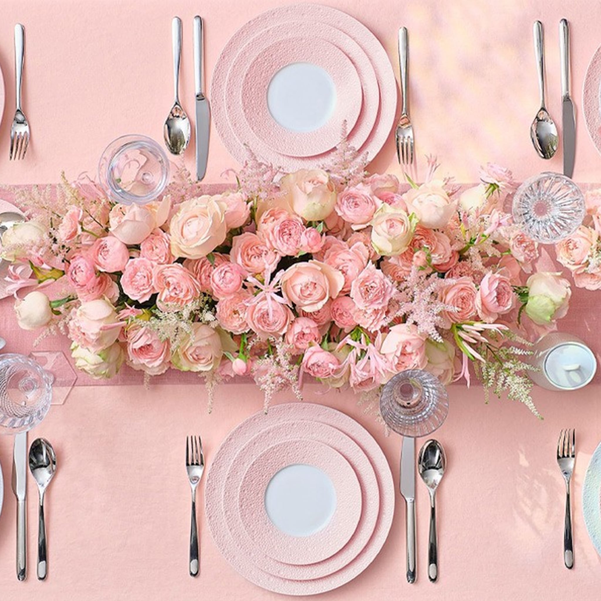 Cena ambientada em mesa, com flores rosas e com pratos da coleção Ecume Rosa.