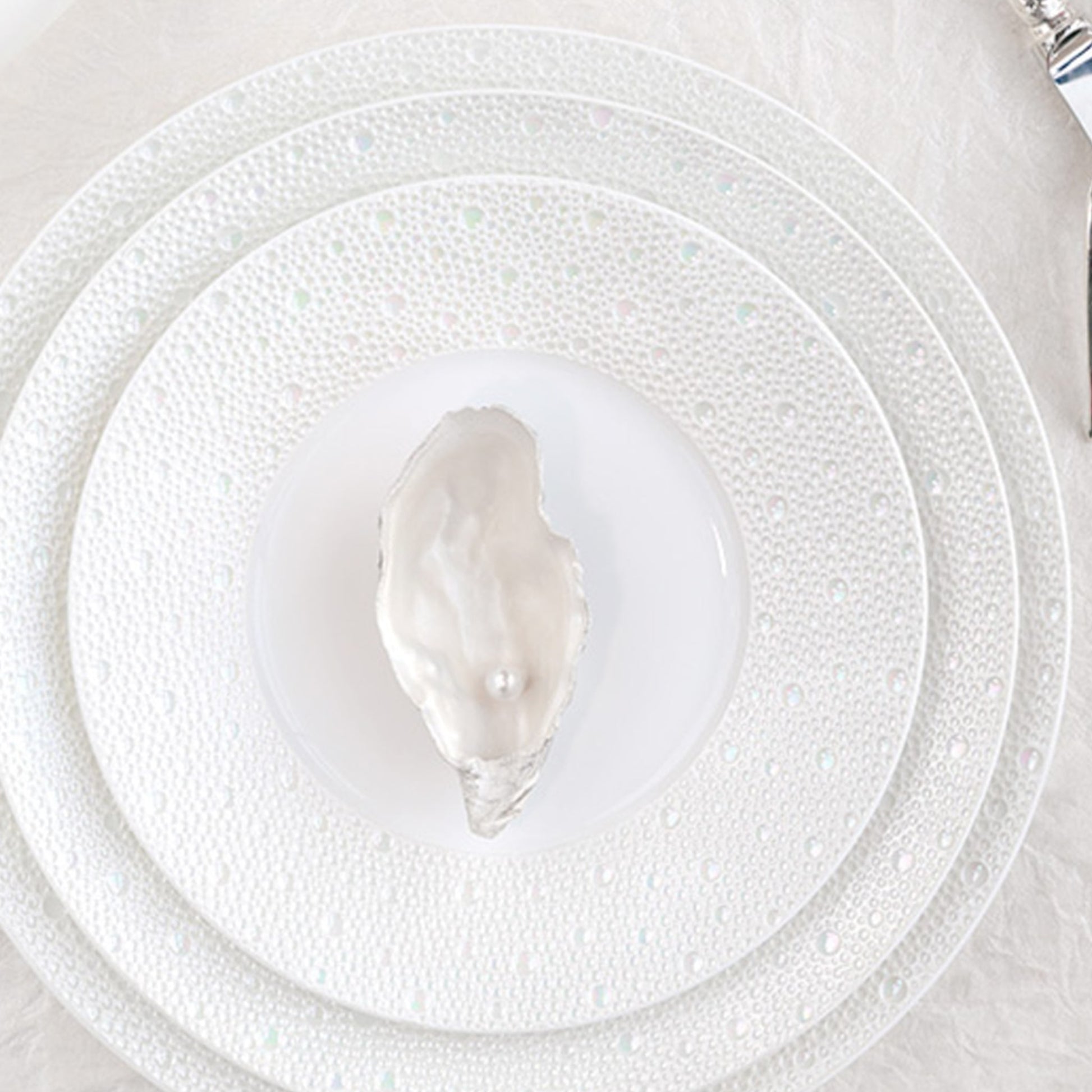 Pratos da coleção Ecume Pérola, com uma ostra e uma pérola dentro.