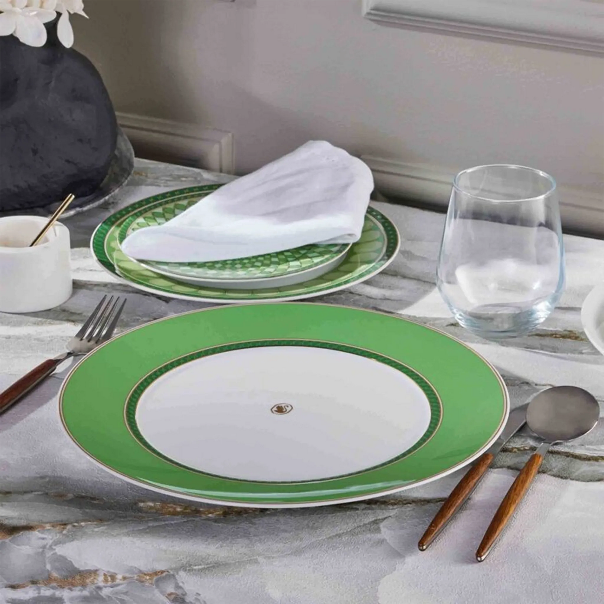 Prato Raso Swarovski Verde ambientado em mesa de pedra com outros utensílios de jantar.