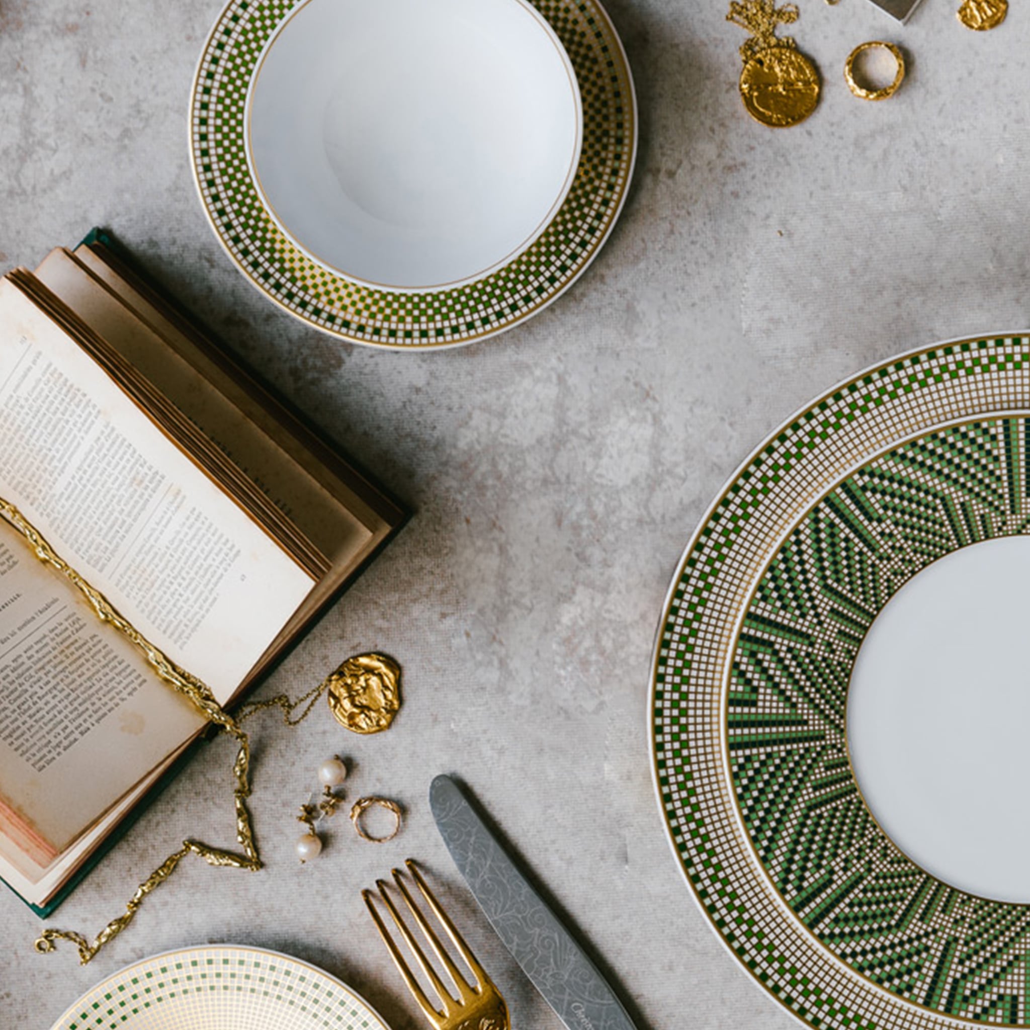 Pratos da coleção Agusta em cima de mesa de mármore com adornos de ouro ao redor.