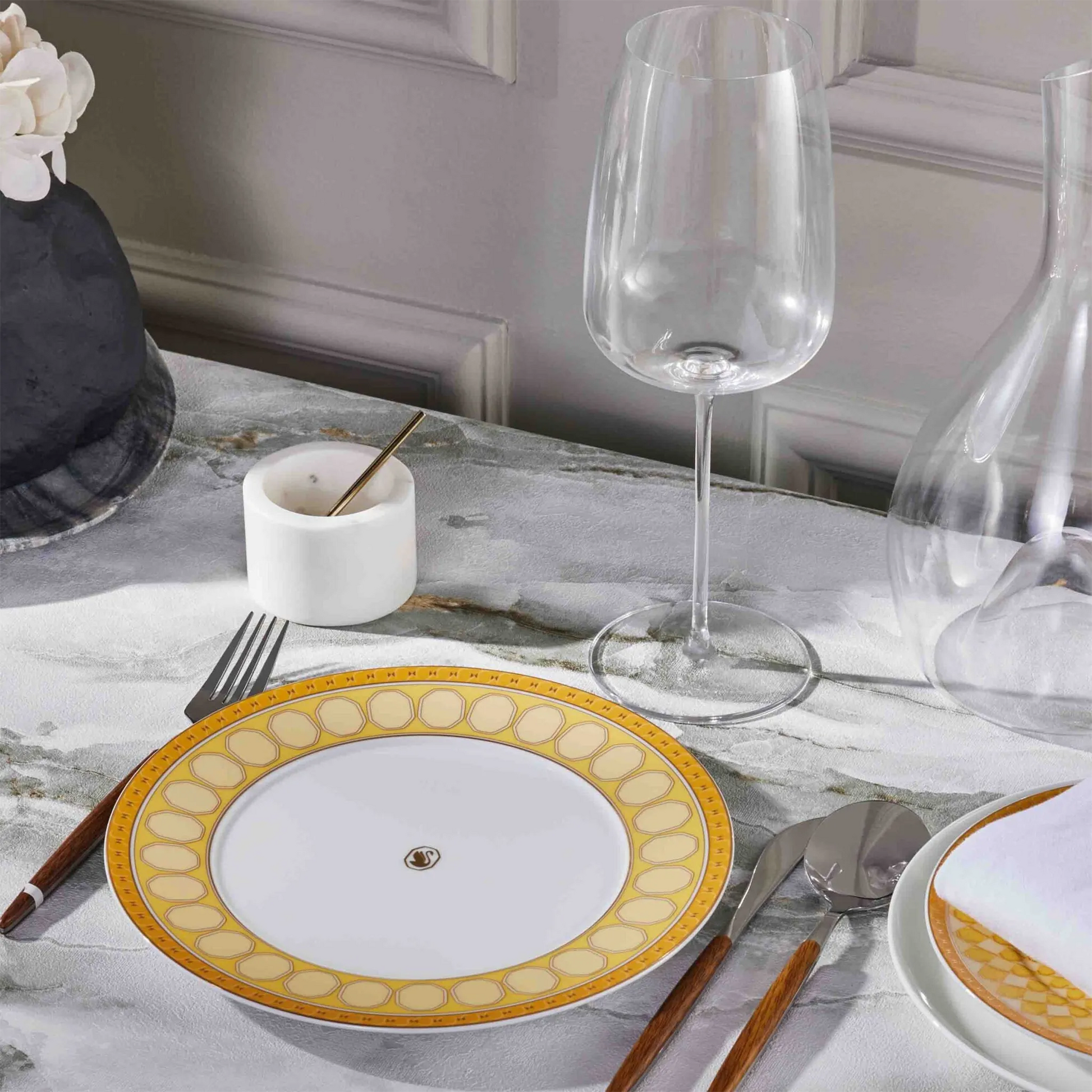 Prato Sobremesa Swarovski Amarelo ambientado em mesa de pedra, com talheres e taça de cristal ao lado.