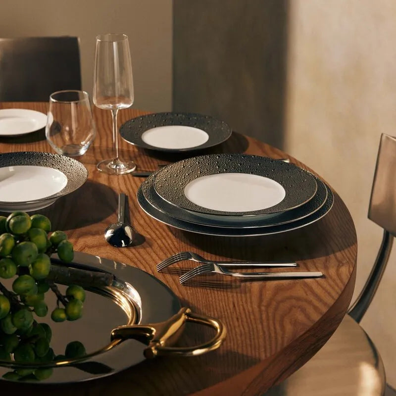 Mesa posta com pratos da marca Bernardaud Limoges, sobre mesa de madeira, com taça e copo de cristal, talheres prateados e bandeja de prata.