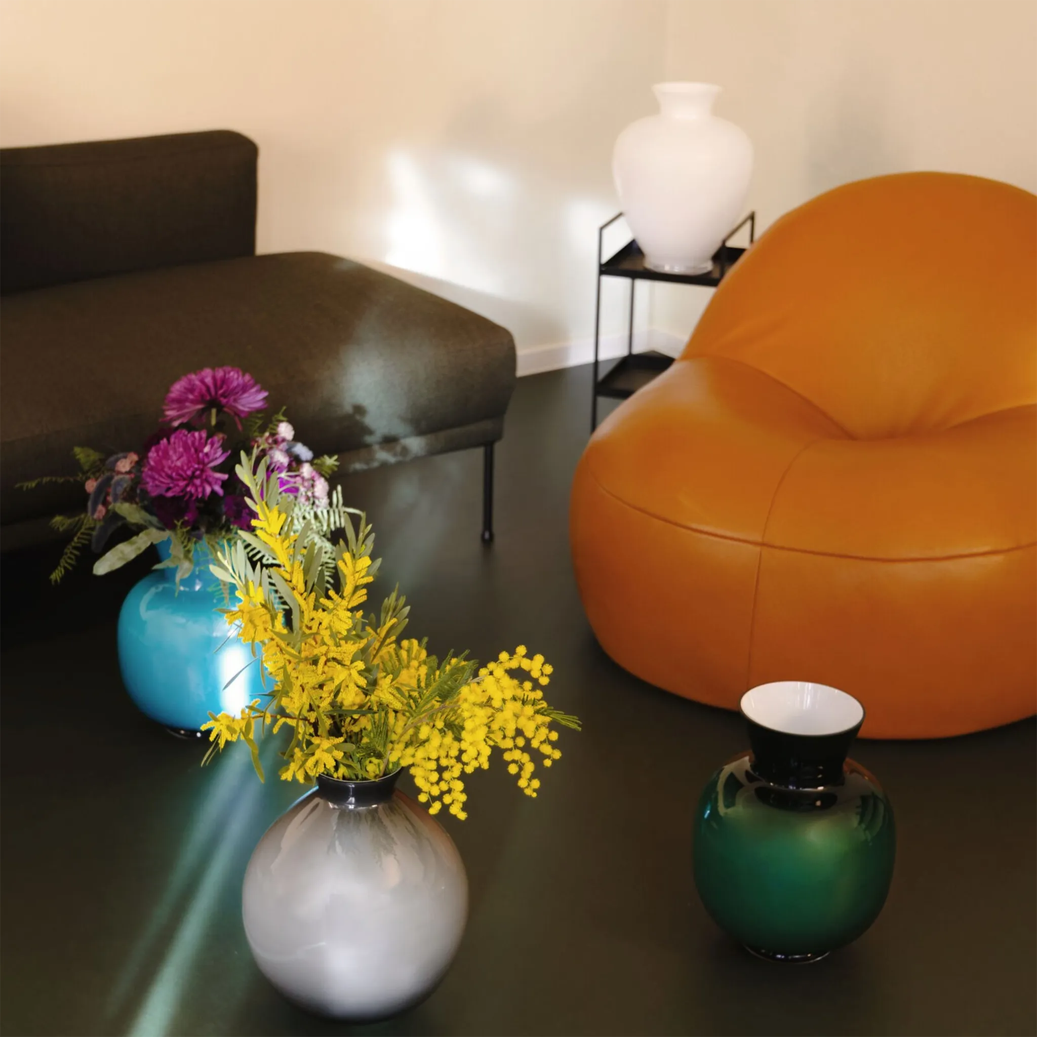 Coleção de vasos Rosenthal dispostos em sala com sofá e poltrona laranja.