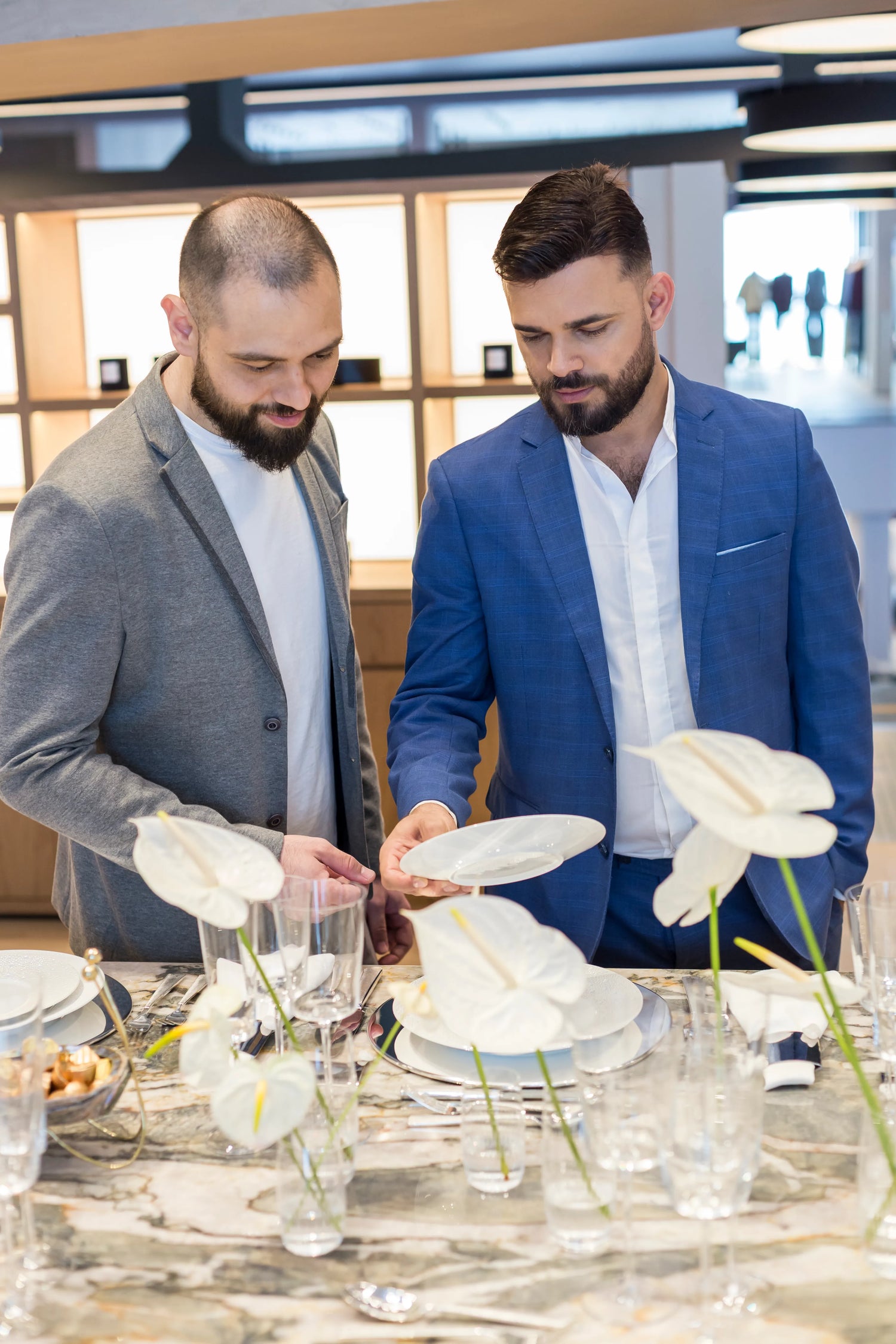 Ramiro e Michael, donos da Celadon, arrumando uma mesa com pratos, copos, taças e talheres vendidos na loja Celadon.