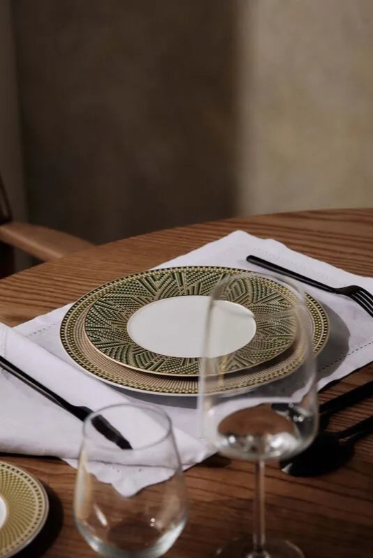 Mesa posta com prato, talheres, taças e guardanapos, sobre uma mesa de madeira.
