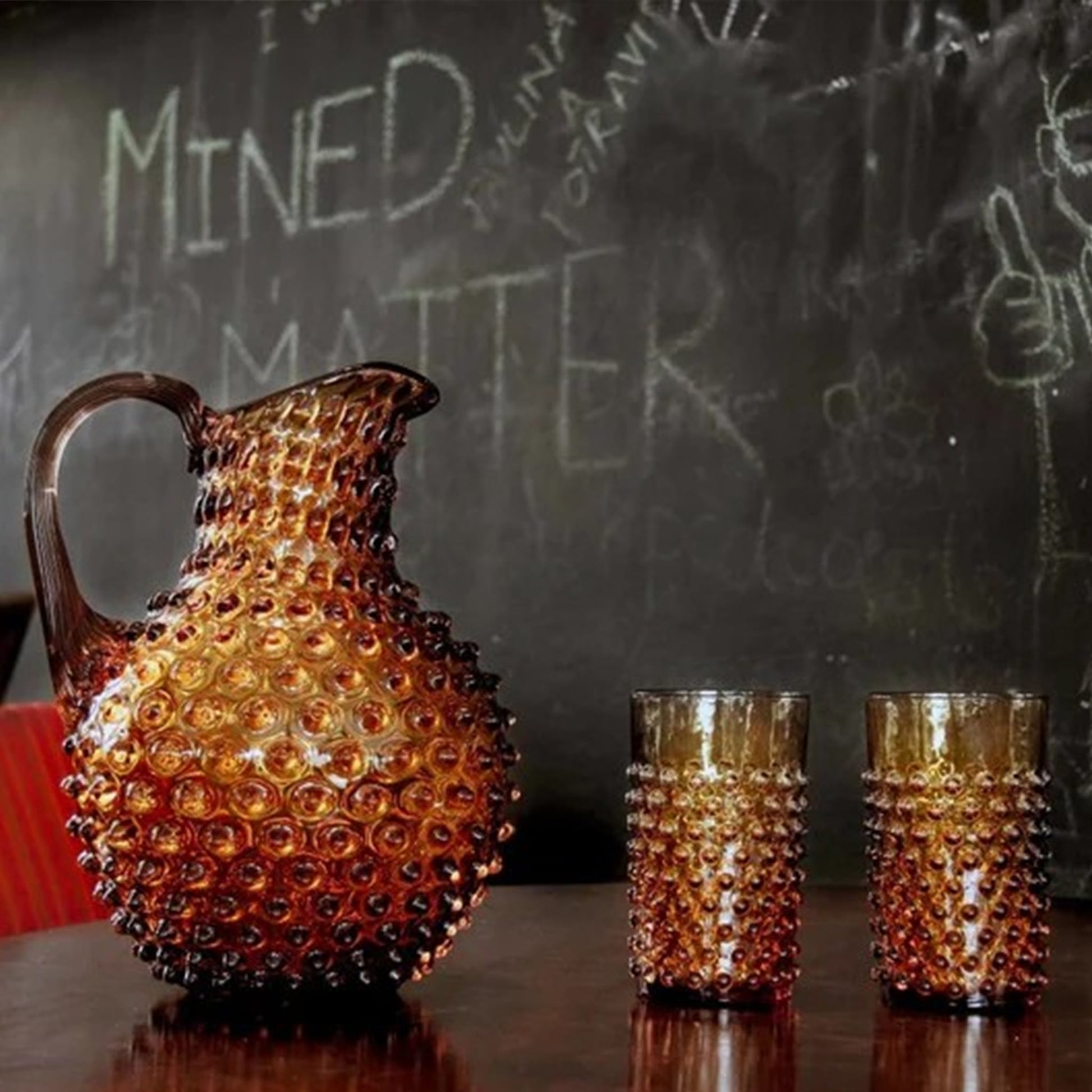 Copo Curto Hobnail Âmbar em cima de uma mesa, com uma jarra da mesma coleção ao lado.