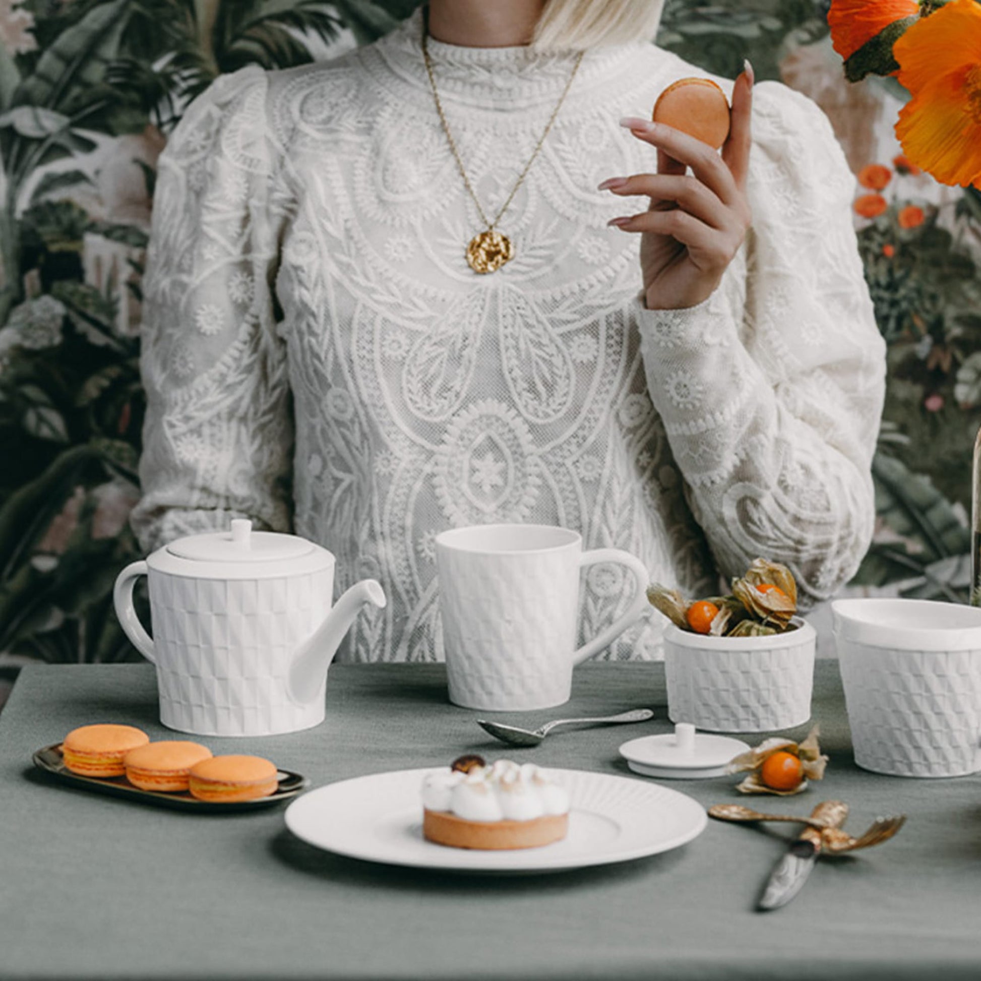 Mulher sentada à mesa, com itens da coleção Twist em sua frente, degustando doces e café.