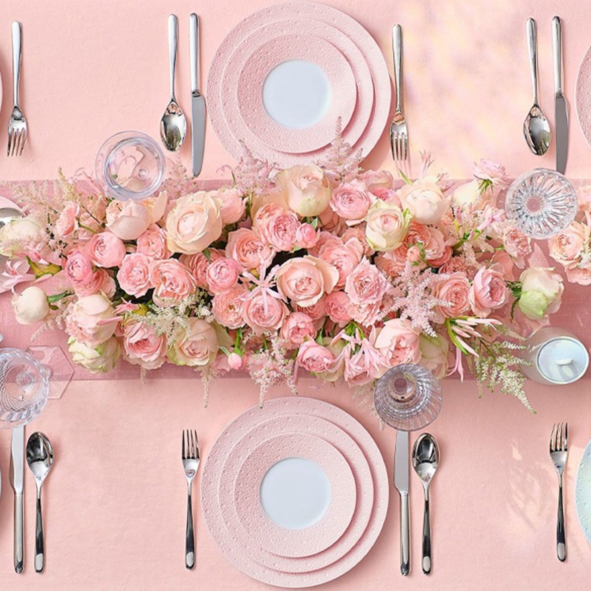 Pratos da coleção Ecume Rosa em mesa com talhes, flores e toalha rosa.