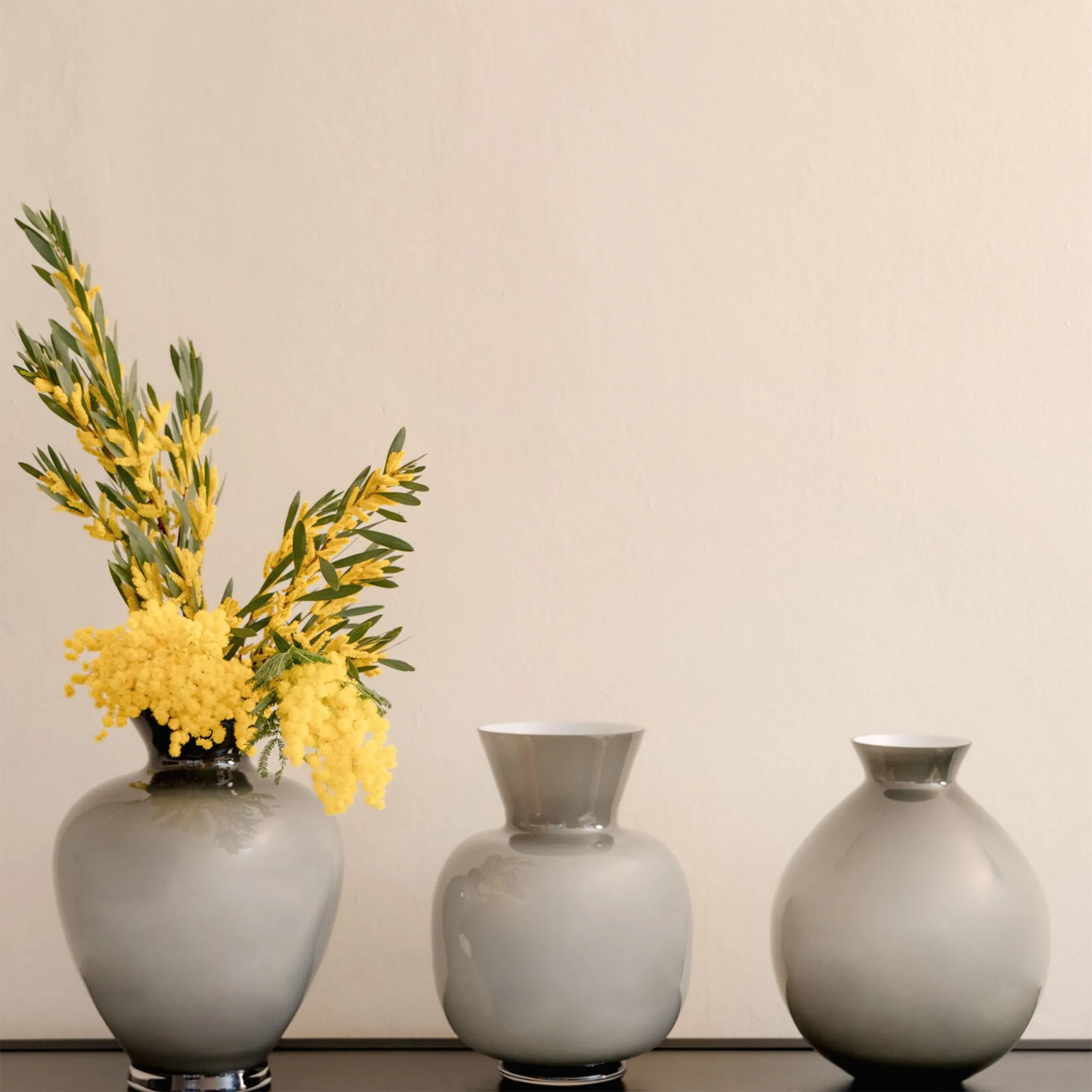 Coleção de Vasos Rosenthal Cinzas em cima de prateleira preta com flores amarelas dentro.